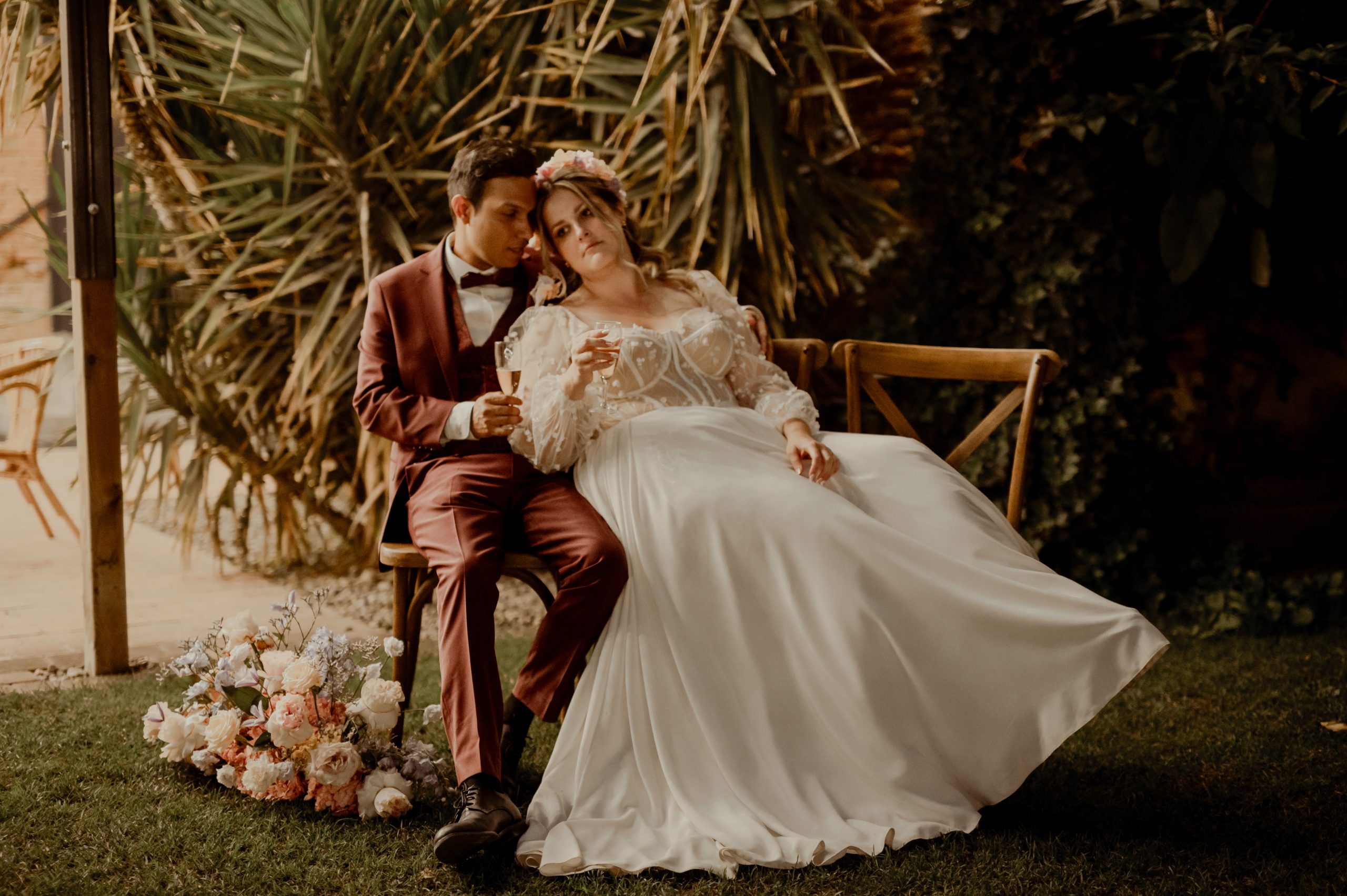 Emma et Maël assis côte à côte lors de leur mariage, la jupe fluide de sa robe de mariée sur mesure déployée autour d'elle.