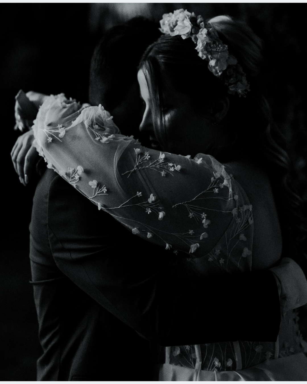 Emma enlace Maël lors de leur mariage, vêtue de sa robe de mariée sur mesure aux manches en tulle brodé.